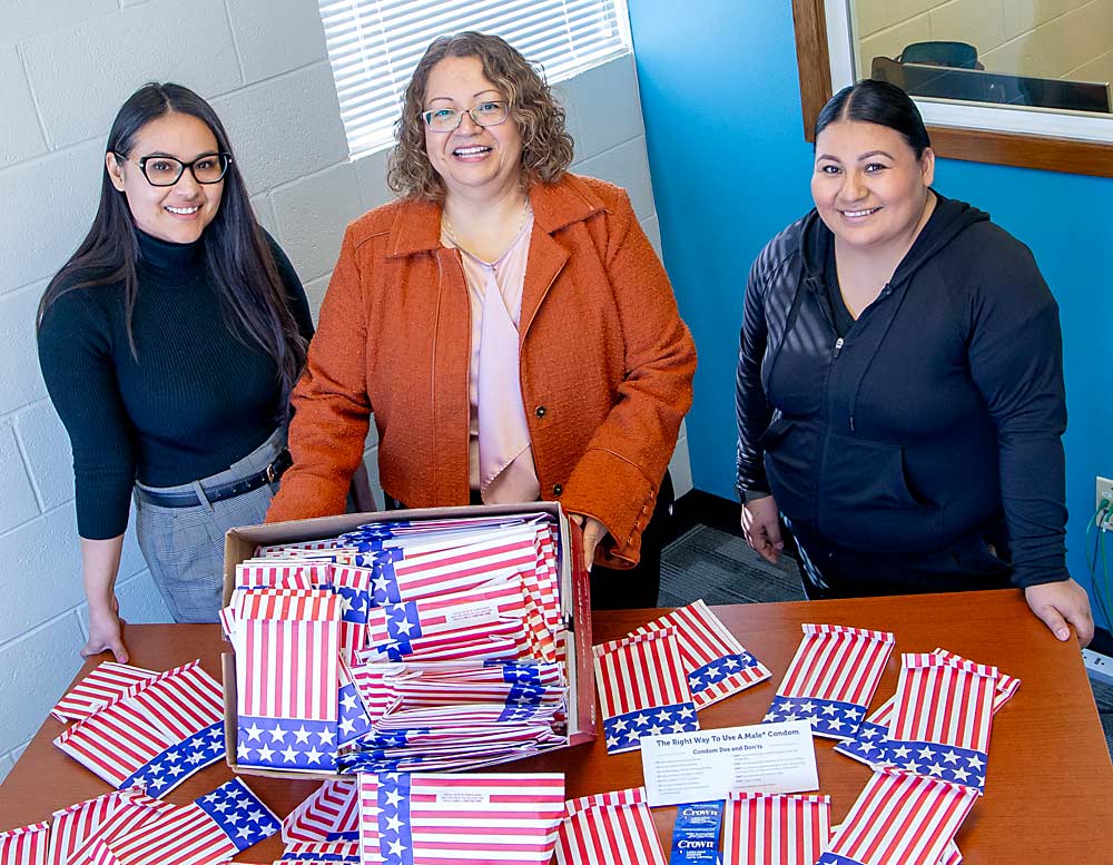 En marzo en el Quincy Community Health Center de Quincy, Washington, las promotoras Priscilla Tovar, Mary Jo Ybarra-Vega y Dalia Ramírez, de izquierda a derecha, posan con “Party Packs” (paquetes de fiesta) los cuales contienen condones e instrucciones para su uso. Este trío de mujeres suele ofrecer los paquetes durante la incorporación de los trabajadores a sus empleos. (Ross Courtney/Good Fruit Grower)