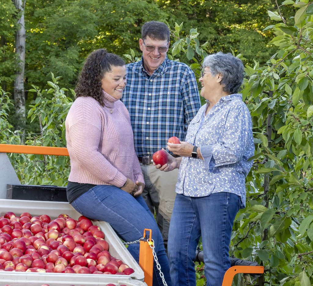 Incluso durante una sesión fotográfica para Good Fruit Grower, la familia DeMarree de Williamson, Nueva York, no puede resistirse a evaluar la calidad de su fruta. Desde la izquierda, Kristen, Tom y Alison DeMarree examinan las manzanas Minneiska (comercializadas como SweeTango) recién cortadas durante la cosecha de septiembre, mientras Alison se dispone a desechar una manzana defectuosa que ha encontrado en la caja. Esa atención al detalle es una de las muchas razones por las que los DeMarree fueron nombrados los mejores productores de fruta del año 2025 por la revista Good Fruit Grower. (TJ Mullinax/Good Fruit Grower)