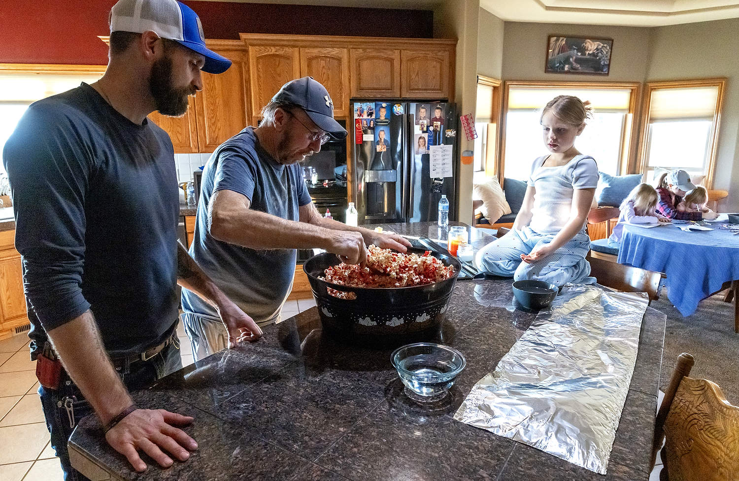 De izquierda a derecha, Matt Eddie, su abuelo Jim Eddie y su hija Sarah preparan palomitas de maíz, mientras su esposa, Leah, y sus hijas Sadie y Faith trabajan en la mesa que se ve al fondo de la fotografía tomada en diciembre. El año pasado, la familia Eddie vendió su huerta, ubicada en Grandview, Washington, después de que las dificultades económicas llevaran a Matt a tener pensamientos suicidas. Tras buscar ayuda, ahora quiere que otros agricultores sepan lo importante que es la salud mental. (TJ Mullinax/Good Fruit Grower)