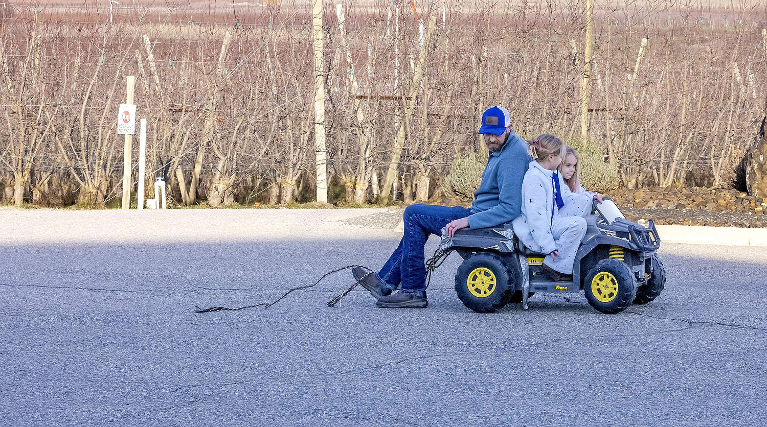 Matt Eddie juega con sus hijas Sarah y Sadie delante de su casa. Ya no se dedica a la horticultura en las huertas que se ven al fondo. Decidieron venderlas, lo que les permitió saldar sus deudas, conservar su casa y priorizar la salud mental de Matt, para que pueda ser un padre cariñoso, según explicó. (TJ Mullinax/Good Fruit Grower)