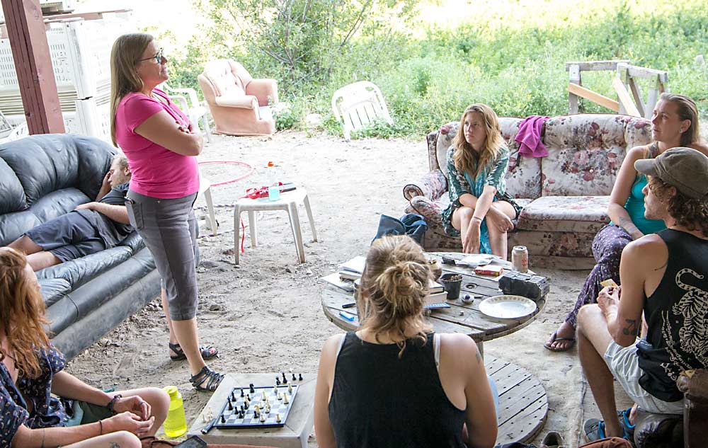 Jan Carlson, standing, discusses contingency evacuation plans in July 2018 with backpacking workers, including Amanda MacKenzie, center on couch, as wildfires burn in the hills surrounding the Carcajou Fruit Co. near Summerland, British Columbia. (Ross Courtney/Good Fruit Grower)