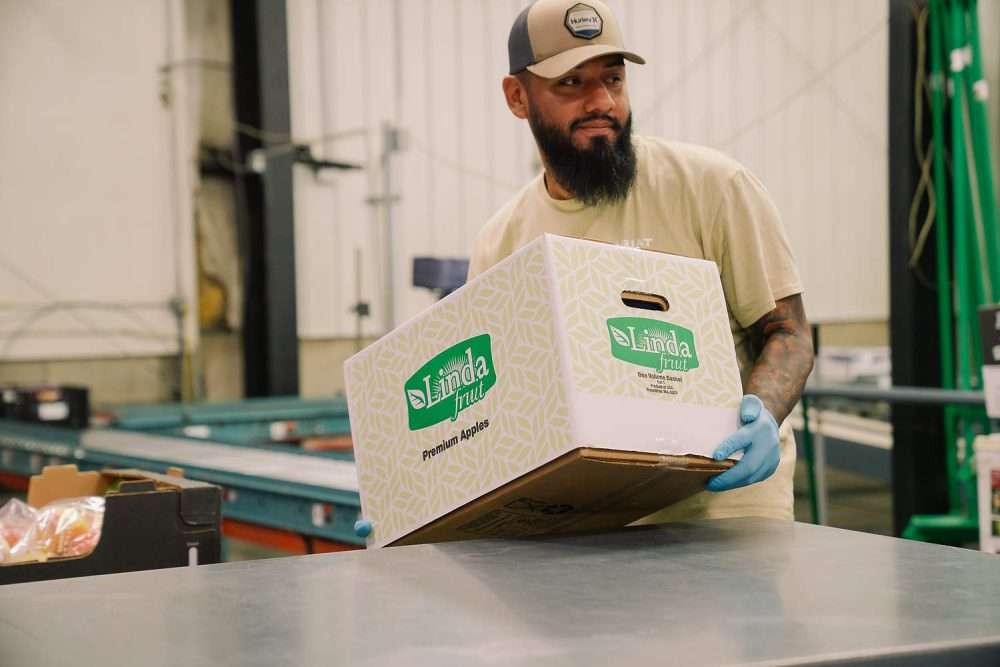 A worker holding a box of apples at Linda Fruit in Wenatchee, Washington.