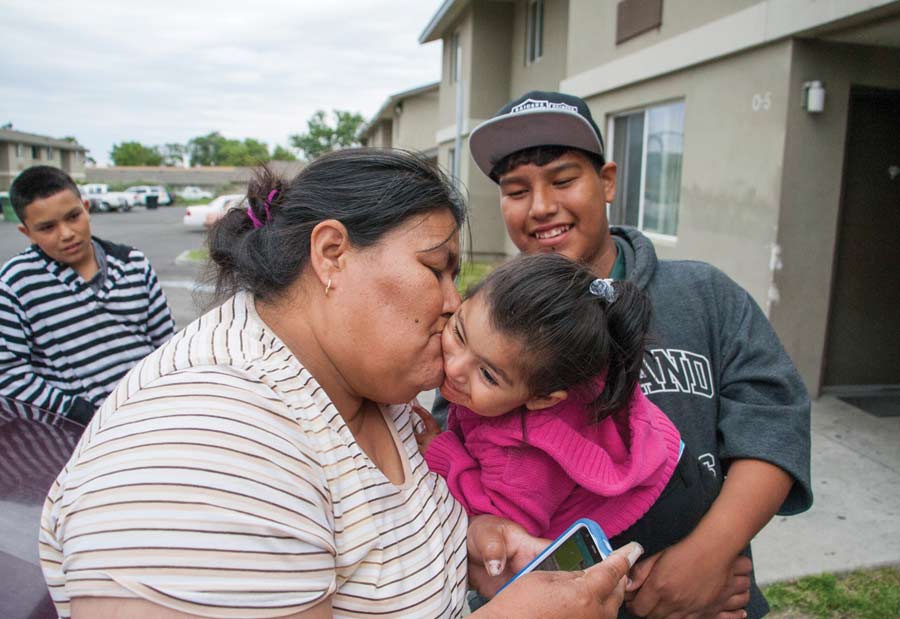 Beatriz Lara bids farewell to her granddaughter Ana Robledo outside Lara’s apartment at the Orchard Homes farmworker housing facility in Milton-Freewater, Oregon, in May. Holding Robledo is Lara’s son Javier Lara. The family lives at the complex year-round while working in nearby orchards. The farmers who own the building would like to use it to house visiting H-2A workers, but their U.S. Department of Agriculture loan requirements restrict the facility to U.S. citizens and permanent residents. <b>(Ross Courtney/Good Fruit Grower)</b>