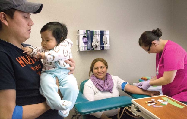 Stemilt Growers employee Alfonso Perez holds his 6-month-old daughter, Lexi Amaya, while wife Claudia Rea has blood drawn March 29, 2016, as part of her wellness exam at the Stemilt Family Clinic in Wenatchee, Washington. <b>(Shannon Dininny/Good Fruit Grower)</b>