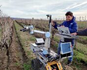 Carnegie Mellon University graduate students Nomaan, left, and Sparsh Garg operate a pruning robot at a Cornell University research vineyard in Portland, New York. Nomaan is teleoperating the small robotic arm that is guiding the movements of the large robotic pruning arm. The researchers are gathering demonstration data to train robots to prune vines more like humans do. (Courtesy Carnegie Mellon University)