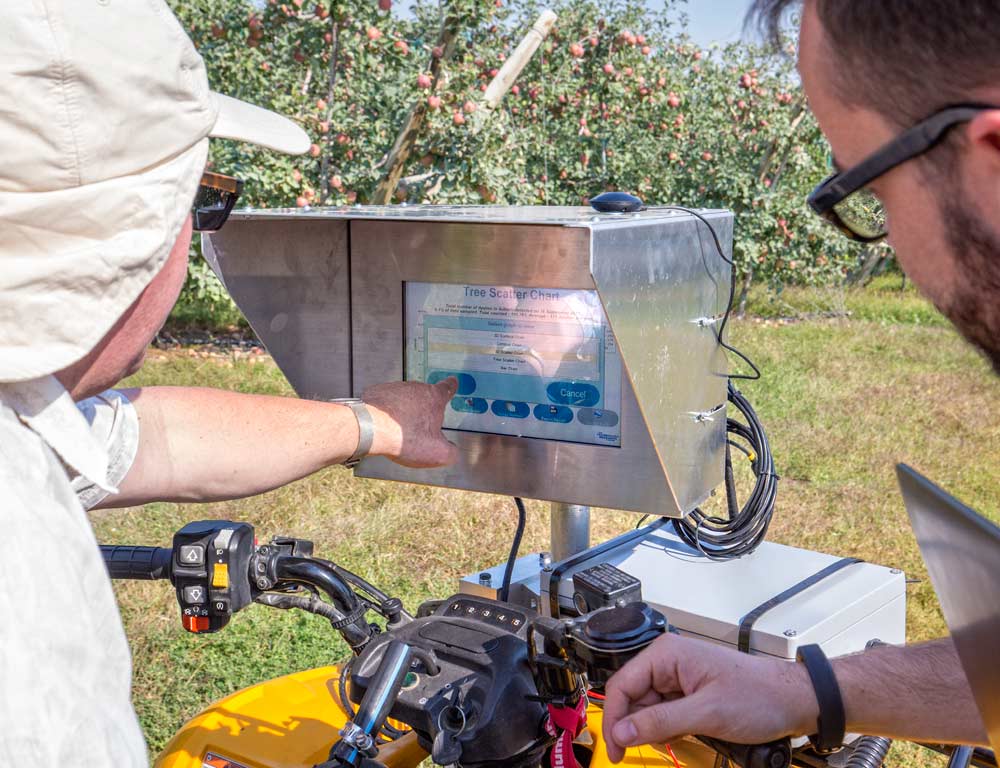 Kurt Scudder, left, and Sam Dingle use the touch monitor to control a PC that operates Intelligent Fruit Vision’s cameras, recommends speed rates to drivers and provides crop load data results in the field. <b>(TJ Mullinax/Good Fruit Grower)</b>