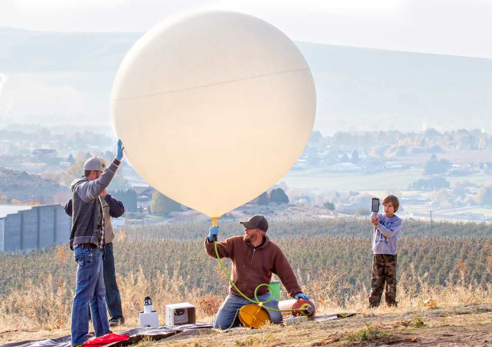 Steve Potter, left, and Jeff Johnston prepare to launch a freshly picked Autumn Glory apple into the upper stratosphere (about 20 miles) above Selah, Washington, while Potter’s son, Eli, livestreams the launch to his classroom on October 23, 2018. This was the second launch of an apple to near-space by Potter and Johnson for Domex Superfresh Growers. (TJ Mullinax/Good Fruit Grower)