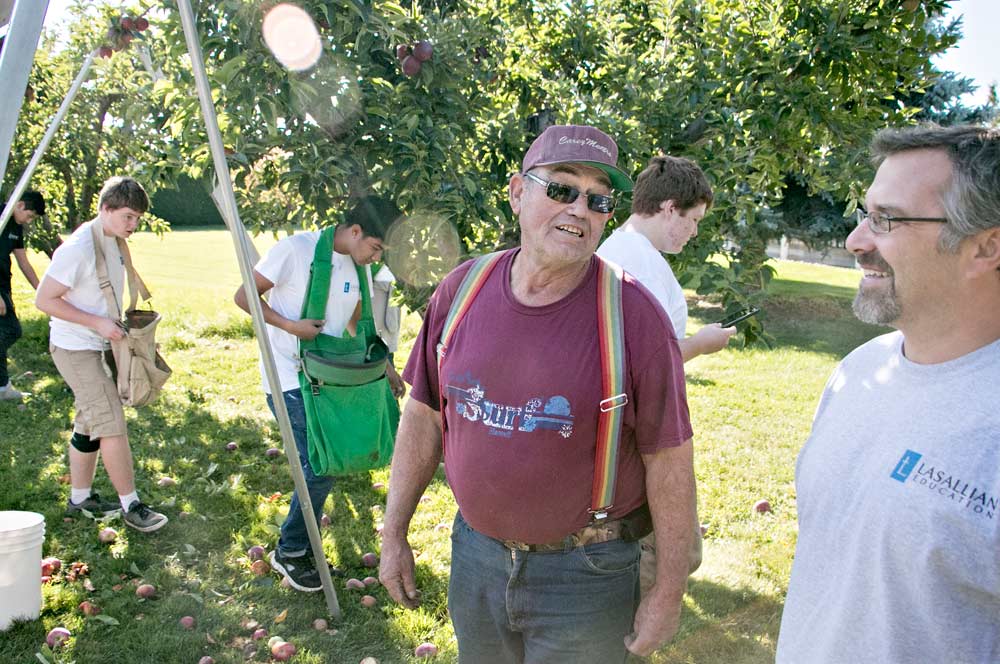 Fourth-generation orchardist Rick Alderson, center in red, said the teenagers’ annual visit has allowed him to keep what remains of his family’s orchard even though he retired from commercial farming years ago. At 69, he wouldn’t be able to pick the apples himself. Here, he talks with math teacher Rick Maib. <b>(Ross Courtney/Good Fruit Grower)</b>