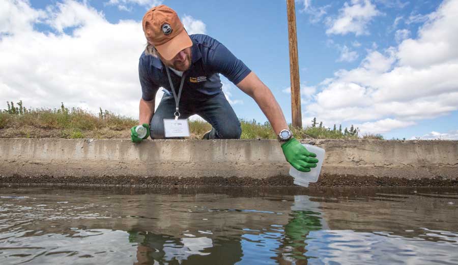 Ronald Bond of the University of California-Davis, shows a proper method for obtaining an accurate water sample during an irrigation water testing workshop in Selah, Washington, in May. Bond said samples should not be taken by skimming the surface or sides of an irrigation canal. Instead, dip the container mouth down into the water and sweep in a half-moon arc to obtain a representative sample. <b>(TJ Mullinax/Good Fruit Grower)</b>
