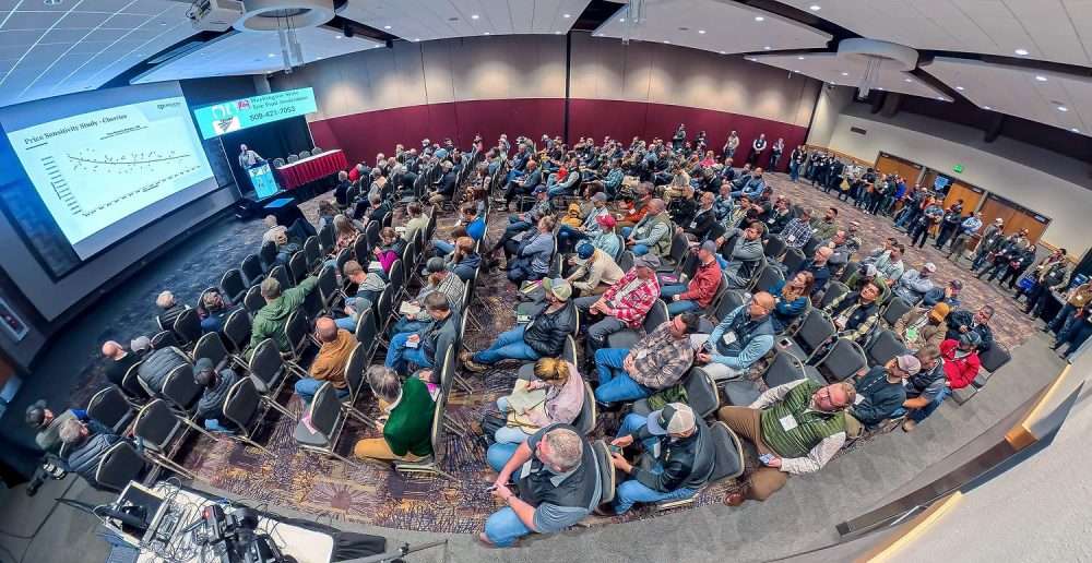 A packed house listens to Welcome Sauer present an analysis of the 2025 cherry season during the second day of the Washington State Tree Fruit Association Annual Meeting, held at the Wenatchee Convention Center Dec. 8–10. (TJ Mullinax/Good Fruit Grower)
