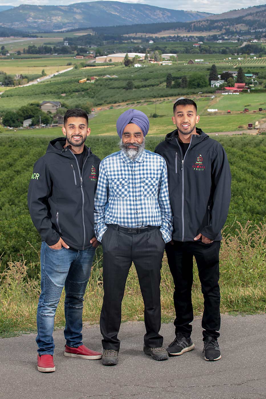 Bill Sandher and his sons, Gurtaj, left, and Prabtaj, with their growing farm and packing facility in the far background. (TJ Mullinax/Good Fruit Grower)