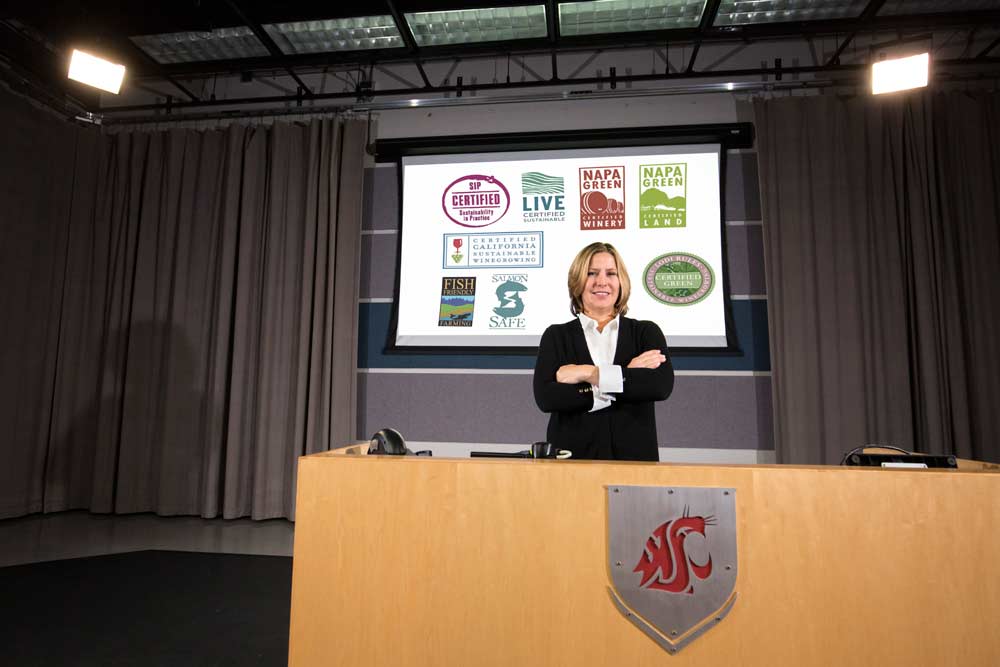Jill McCluskey, an economist at Washington State University, says many of the organic or sustainability certifications, such as those behind her, may increase wine ratings but confuse consumers. (TJ Mullinax/Good Fruit Grower photo illustration)