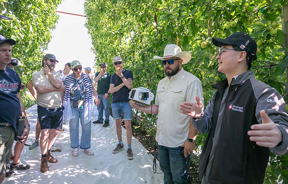 Pedro Cuevas Jr. holds Orchard Robotics’ latest vision system while Charlie Wu, right, talks about the technology as the Orchard of the Future tour group visits an Allan Bros. orchard in the Yakima Valley. (TJ Mullinax/Good Fruit Grower)